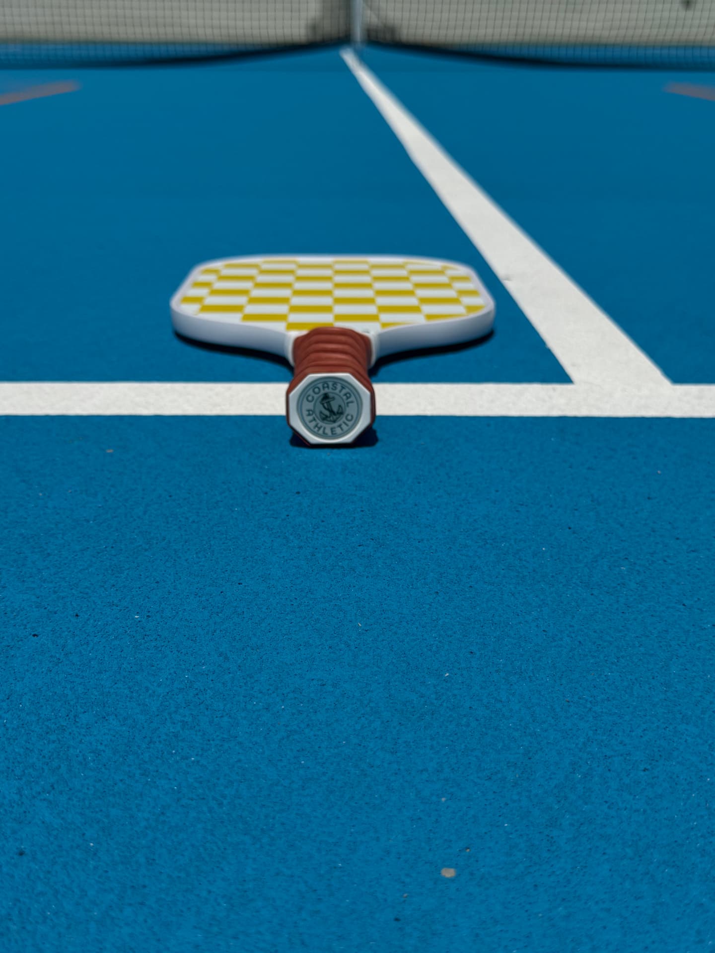 Sunrise Key paddle resting on a blue South Florida court